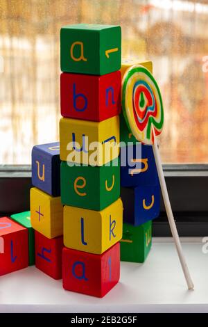 Ein Turm aus bunten Holzspielzeugblöcken mit Buchstaben und Zahlen bilden das Wort 'abuela' (Oma) mit einem Lollipop von Ein Fenster Stockfoto