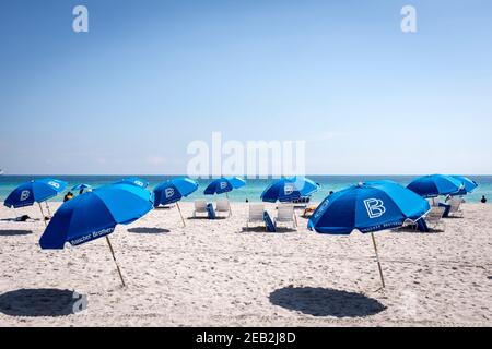 Blaue Sonnenschirme in gepflegten Linien gegen das azurblaue Wasser des Atlantiks vor South Beach, Miami Beach, Florida angeordnet Stockfoto