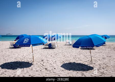 Blaue Sonnenschirme im Sand gegen das azurblaue Wasser des Atlantiks vor South Beach, Miami Beach, Florida Stockfoto