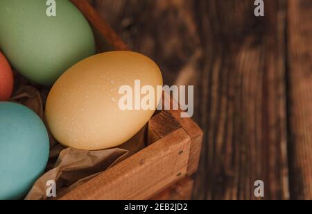 Bunte ostereier aus nächster Nähe. Holzkiste mit farbigen Ostereiern auf dunkelbraunem Hintergrund. Stockfoto