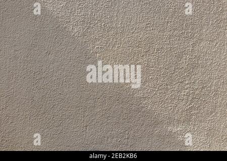 Ein Schatten fällt diagonal über die raue Oberfläche einer verputzten, gelblich-weißen Wand, um einen abstrakten, grungen Hintergrund zu schaffen. Stockfoto