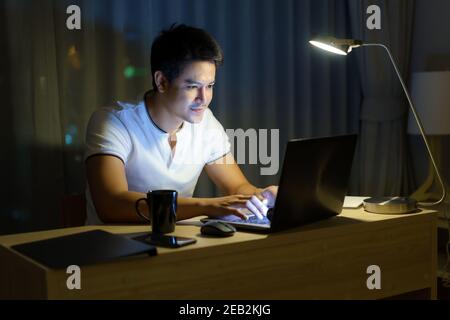 Asiatische Mann arbeiten zu Hause sitzen vor einem Computer spät in der Nacht. Stockfoto