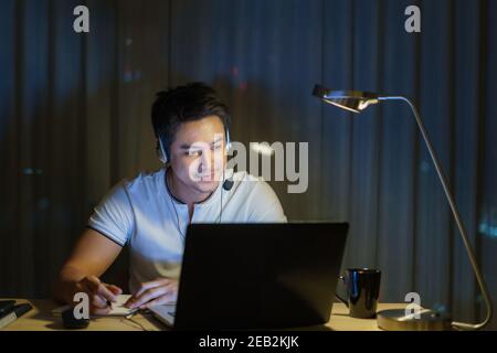 Asian Mann Arbeit zu Hause sitzen bei der Arbeit mit Kollegen oder Managern per Videoanruf in der Nacht zu Hause. Stockfoto