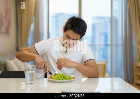 Ein asiatischer Mann isst ein amerikanisches Frühstück im Wohnzimmer zu Hause. Stockfoto