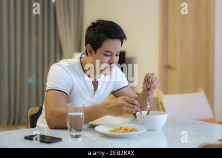 Ein asiatischer Mann ist Abendessen allein am Esstisch in der Nacht zu Hause essen. Stockfoto