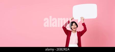 Lächelnde junge asiatische Frau hält leere Sprechblase in rosa Banner-Hintergrund mit Kopierbereich Stockfoto