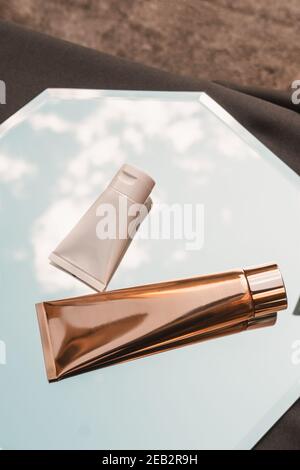 Zwei weiße und goldene Kosmetikröhren auf Spiegelhintergrund, Beauty-Produkt, Branding-Paket Mockup, minimalistisch, Draufsicht Stockfoto