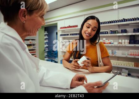 Leitender Apotheker zeigt jungen Kunden den Bildschirm eines digitalen Tablets Flasche mit Nahrungsergänzungsmitteln in der Apotheke halten Stockfoto