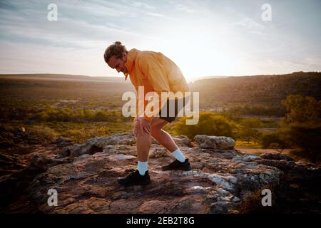 Hübscher junger Athlet, der das Knie hält, während er Schmerzen im Knie spürt Beim Laufen in der Natur Stockfoto