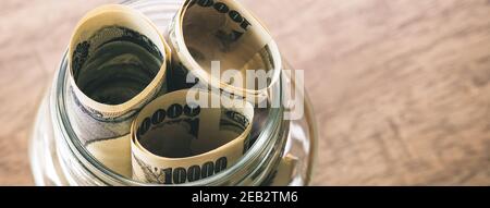 Rollen von japanischen Yen-Geldscheinen in der gehalten Glas Glas auf Holz Tisch Banner Hintergrund Stockfoto