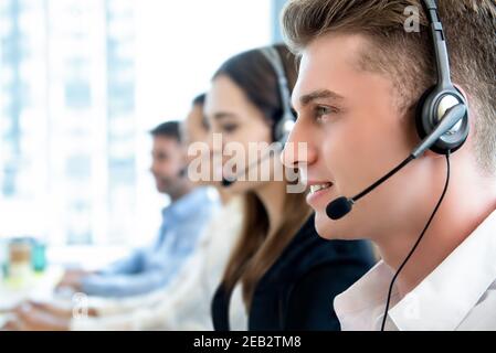 Lächelnder, freundlicher Mann, der mit dem Team im Callcenter arbeitet Als Telemarketing-Kundendienstmitarbeiter Stockfoto
