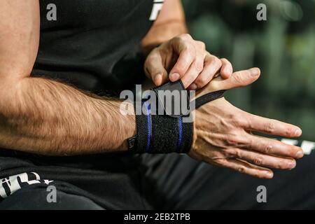 Nahaufnahme der Hände eines unbekannten Mannes, der hält und setzt Auf und Anpassung Wrap Bandagen an den Handgelenken für Powerlifting Körper Gebäude Training Sportausrüstung Stockfoto