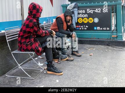 Männer sitzen draußen auf einer Bank in der Nähe einer U-Bahn-Station in Manhattan. Stockfoto