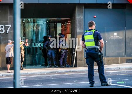 Ein Polizeibeamter steht auf der Straße, während sich die Beamten der Taktischen Polizeieinheit am Eingang des Gebäudes verstecken. Ein Vorfall in Melbournes innerem Vorort Prahran löste eine große Reaktion der Polizei aus, an der die Special Operation Group und ein Dutzend Polizisten beteiligt waren, als sie auf einen jungen Mann reagierten, der Steine auf die Straße schleuderte, als er ein Wohngebäude auftaute. Ein Schaden an Eigentum und Straße mit Steinen und Trümmern bedeckt gestoppt Donnerstag Morgen Verkehr für eine Stunde und eine Hälfte. Nach einer langen Verhandlung mit der Polizei gab sich der Täter der Polizei hin und er wurde mit dem Krankenwagen gebracht, um seine Schnitte zu behandeln Stockfoto