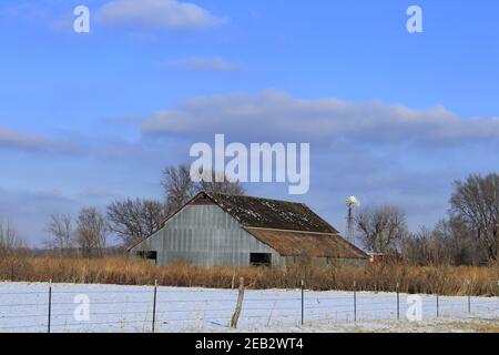 Kansas Country Barn mit Schnee, Zaun, blauem Himmel und Wolken im Land, das hell und bunt ist. Stockfoto