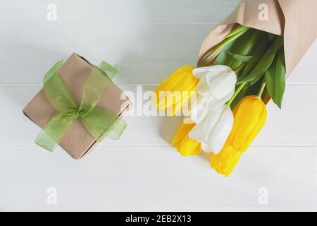 Gelbe und weiße Tulpen auf hellem Holzhintergrund. Geschenk und Blumenstrauß in Kraftpapier. Das Konzept des Internationalen Frauentags, 8. März, 1 Tag der spr Stockfoto