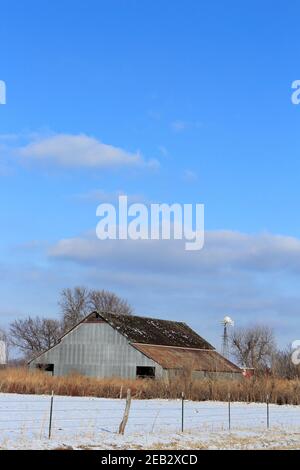 Kansas Country Barn mit Schnee, Zaun, blauem Himmel und Wolken im Land, das hell und bunt ist. Stockfoto