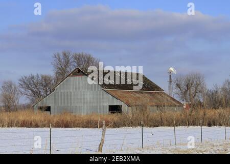 Kansas Country Barn mit Schnee, Zaun, blauem Himmel und Wolken im Land, das hell und bunt ist. Stockfoto