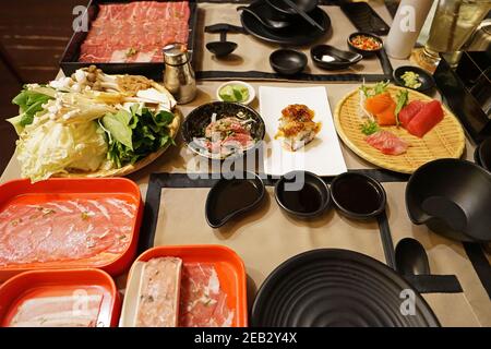 Ein Tisch voller vorbereiteter Teller mit frischem Gemüse, geschnittenem Wagyu-Rindfleisch, Schweinefleisch, Sushi und Sashimi für Shabu Shabu (japanischer Hot Pot) Stockfoto