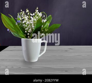 Frühling Stillleben mit zarten Lilien des Tales und Vergiss-mich-nicht Blumen in weißem Becher auf Holztisch. Der Blumenstrauß der Maiglöckchen blüht auf Stockfoto