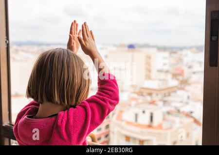 Ein blondes kleines Mädchen applaudiert medizinisches Personal aus ihrem Fenster Während der Coronavirus-Pandemie Stockfoto
