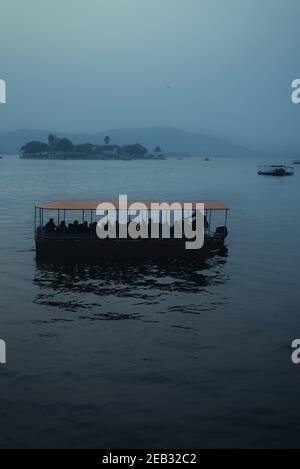 Ein orangefarbenes Boot mit Silhouetten von Menschen auf einem launischen Mystischer See Stockfoto