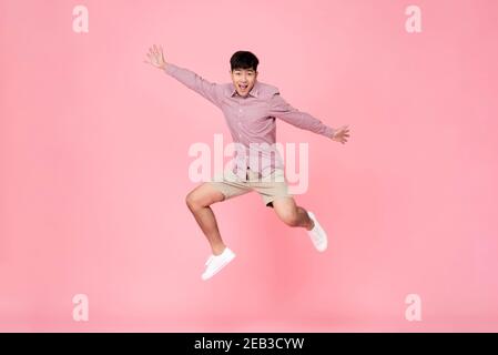 Energetisch glücklich lächelnd junge asiatische Mann in lässigen Kleidung springen studioaufnahme isoliert in farbenprächtigem rosa Hintergrund Stockfoto