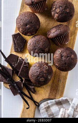 Schokoladen-Muffins. Süße dunkle Cupcakes mit Schokolade und Vanilleschoten auf Schneidebrett. Draufsicht. Stockfoto