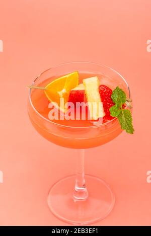 Buntes Fruchtpunsch-Cocktail-Getränk in Coupé-Glas auf Koralle Rosa Hintergrund Stockfoto