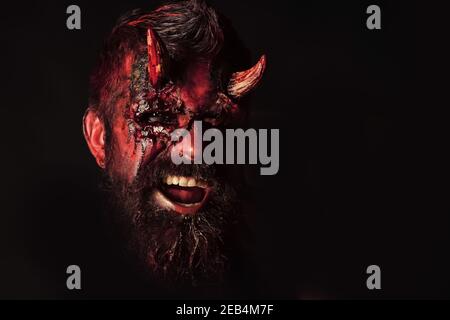 Halloween Teufel. Dämon mit blutigen Hörnern, Augen, rotem Blut, Wunden. Dunkelheit und Licht Konzept. Mann böse hält Kürbis auf schwarzem Hintergrund Stockfoto