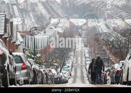 Ein Paar, das vom Hügel in Crouch End Area, London, mit einer Kulisse von Reihenhäusern, die von Schnee bedeckt sind, hinuntergeht Stockfoto