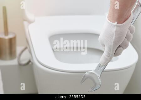 Hand halten Schraubenschlüssel Werkzeug auf Toilettensitz Hintergrund Stockfoto