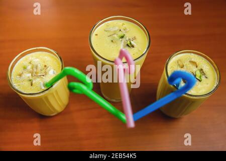 Hausgemachte frische Mango Lassies mit Nüssen und Strohhalmen auf dem Tisch. Süßer Mango Lassi, kalte Sommergetränke Stockfoto