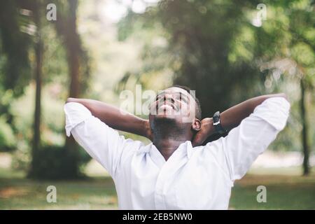 Afrikanischer Geschäftsmann lächelt und steht auf grünem Natur Hintergrund Mit den Händen über dem Kopf Stockfoto