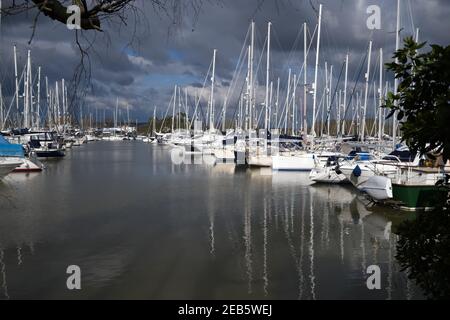 Yachten in Chichester Marina mit Spiegelungen von Masten im Wasser und dramatischen Wolken im Hintergrund. Stockfoto