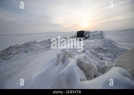 Xilinhot. Februar 2021, 11th. Ein Shuttle-Bus zur Konverterstation Xilingol À800-Kilovolt fährt auf einer verschneiten Straße in der Autonomen Region Innere Mongolei im Norden Chinas, 11. Februar 2021. Alle 59 Arbeiter der Convertor Station entschieden sich, in der Grünland-Region das diesjährige Frühlingsfest zu feiern. Am Vorabend des chinesischen Neujahrsfestes hielten etwa 20 Angestellte an ihren Posten fest, während die, die eine Pause machten, Knödel machten und die Konverterstation mit Papierschneidedekorationen und Pappeln dekorierten. Quelle: Liu Lei/Xinhua/Alamy Live News Stockfoto