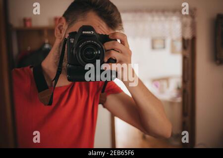 BRCKO, BOSNIEN UND HERZEGOWINA - 16. Oktober 2019: Mann im roten Hemd, der mit Canon 6D ein Selbstporträt im Spiegel macht Stockfoto
