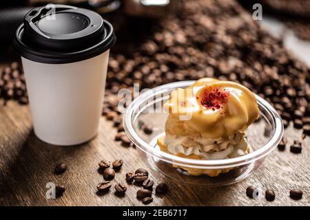 Ein Café zum Mitnehmen mit einem Papierbecher mit schwarzem Plastikdeckel und einem Karamellkuchen in einer Plastikteller bereit für eine Lieferung. Stockfoto