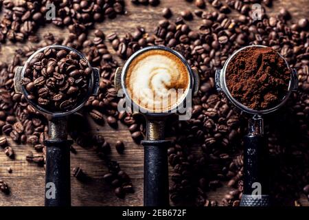 Kaffee in seinen verschiedenen Formen von Rohbohnen bis zu gemahlenem Kaffee und Cappuccino in drei Portafiltern. Stockfoto