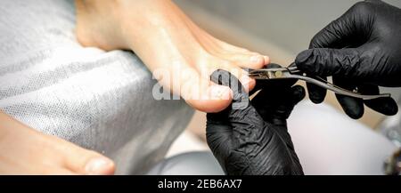 Nahaufnahme eines Pedikürenmeisters ist das Schneiden und Entfernen der Nagelhaut Mit Nagelzange auf weiblichen Zehen in einem Nagelstudio Stockfoto