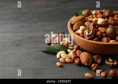 Holzschale mit verschiedenen leckeren Nüssen auf grauem Holzhintergrund Stockfoto