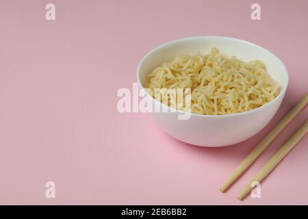 Schüssel mit Nudeln und Essstäbchen auf rosa Hintergrund Stockfoto
