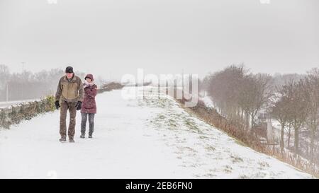 Ede, Niederlande- Ferburary 8, 2021: Älteres Paar, das im Schnee auf einem Deich in Ede, Gelderland, Niederlande, läuft Stockfoto