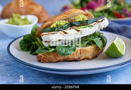 Croissant-Sandwich mit gegrilltem Halloumi-Käse, Rucola und gegrillten Zucchini, blauer Betonhintergrund. Gesundes Frühstück oder Mittagessen. Nahaufnahme. Selecti Stockfoto