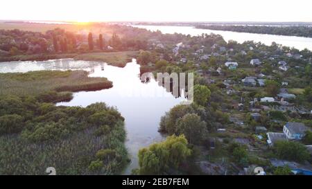 Drohne fliegen über winkenden Fluss umgeben von lokalen Dorf mit Verschiedene Gebäude und Feuchtgebiet und Sumpflandschaft Lebensraum mit einem reedbed Von Common Reed Luftaufnahme Stockfoto