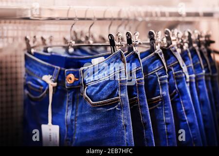 An Metallbügeln hängen blaue klassische Fashion Jeans in verschiedenen Größen. Bekleidungsverkäufe im Einkaufszentrum. Lässiger Style. Stockfoto