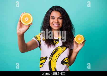 Foto von positiven dunklen Haut Mädchen halten zwei halb in Scheiben geschnitten Orange tragen rosa Banane pring T-Shirt isoliert über teal Farbe Stockfoto