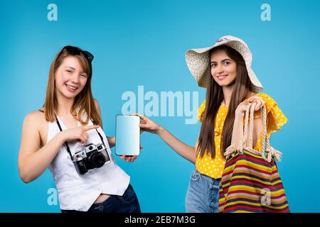 Junge attraktive Touristen halten ein Tablet mit einem weißen Bildschirm, zeigen mit einem Zeigefinger auf den Bildschirm, wo Ihr Text sein kann. Reisen Stockfoto