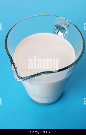 Glaskaraffe mit frischer Milch isoliert auf blauem Hintergrund mit Schatten. High-Angle-Ansicht Stockfoto