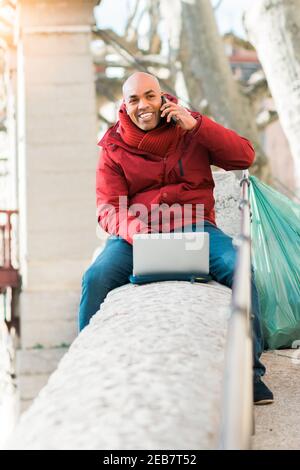 Glücklich lächelnd hispanischen Mann mit einem Laptop-Computer während des Sprechendes Am Telefon Stockfoto